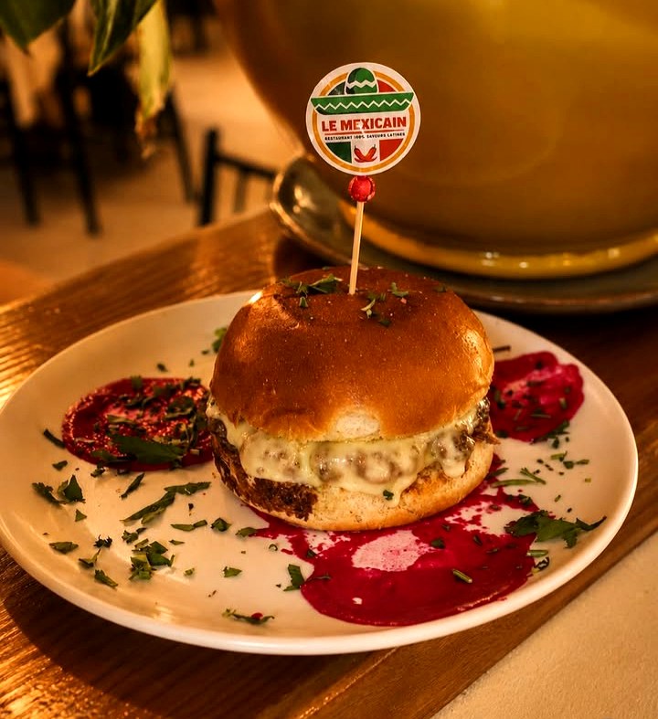 Burger maison nappé de fromage fondu, servi sur assiette avec coulis