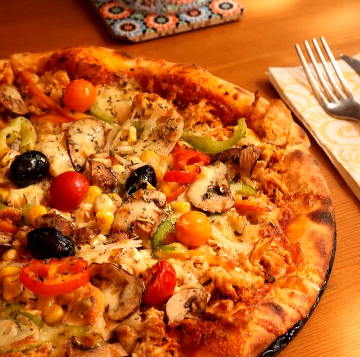 Pizza artisanale garnie de poulet, maïs, olives et légumes